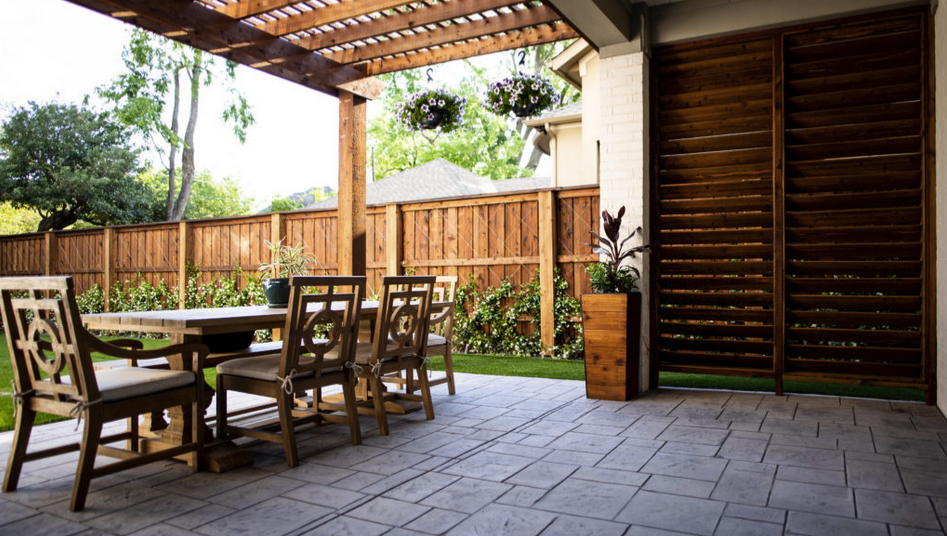 Outdoor patio with wooden dining furniture under a pergola next to a privacy screen.